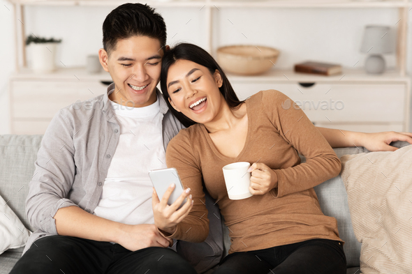 Asian couple resting at home, using phone