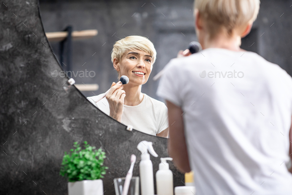 Mature Lady Using Cosmetic Brush Applying Face Powder In Bathroom