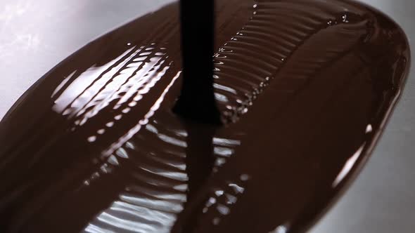 Close-up of Liquid Chocolate Pouring on a Metal Table in a Modern Pastry Shop. alt