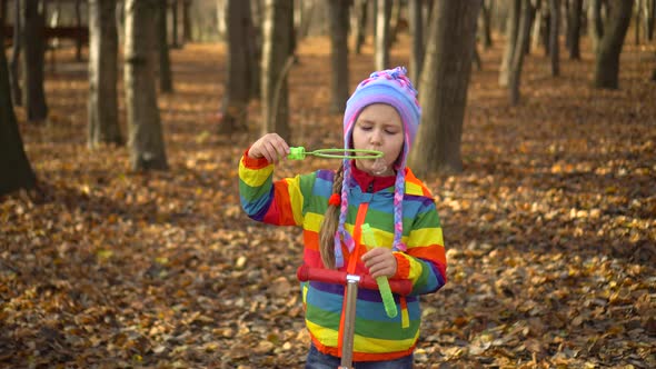 A little girl in a colored jacket and hat blowing bubbles in the autumn Park