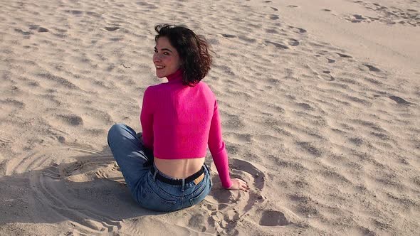 Young Woman Sitting on Sand and Laughs