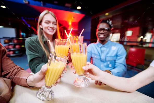 Four intercultural young friends clinking with glasses of fresh orange juice