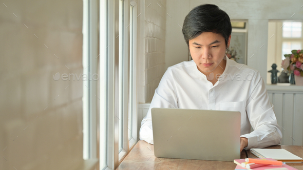 Young asian man is working at home with his laptop to protect against Corona virus or Covid-19.