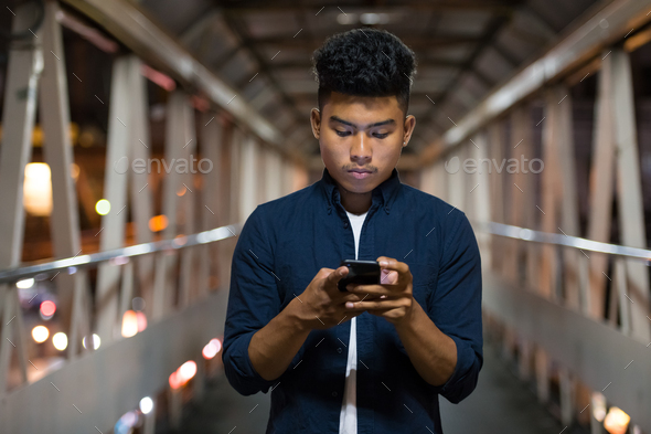 Young Asian man using phone on the footbridge at night