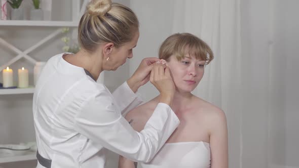Middle Shot of Professional Serious Acupuncturist Inserting Needles Into Ear of Concentrated Asian alt