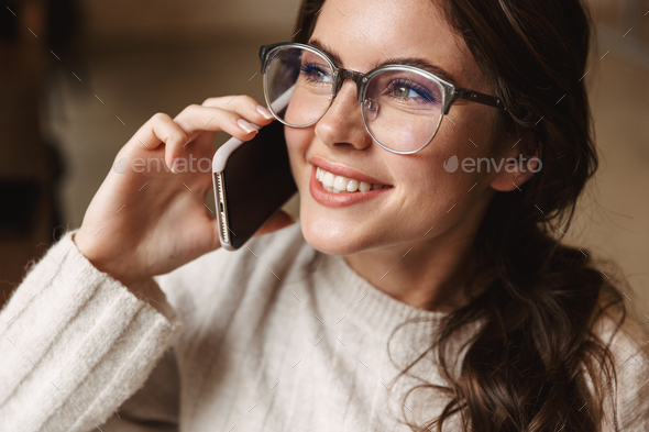 Image of young woman wearing eyeglasses talking on smartphone in cafe