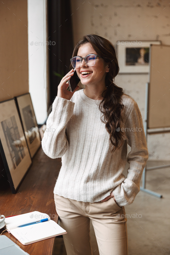 Image of young woman talking on smartphone while working in cafe