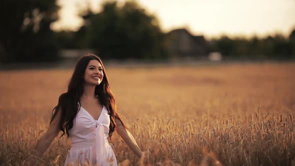 Beautiful Young Woman Enjoys Life Walking on a Wheat Field at Sunset