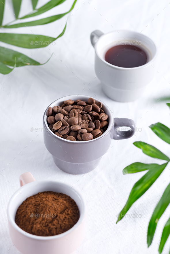 Ceramic cups with freshly roasted coffee beans and fresh ground aromatic coffee on a light