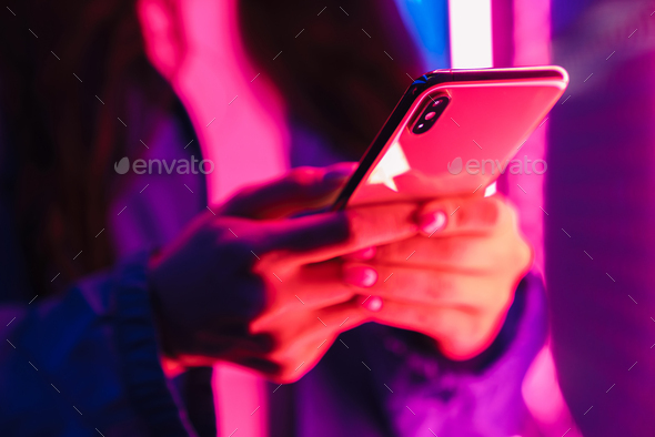 Woman posing over neon lights using mobile phone.