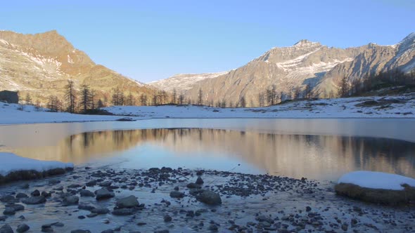 Winter River Flowing to Frozen Mountain Lake in Italian Alps