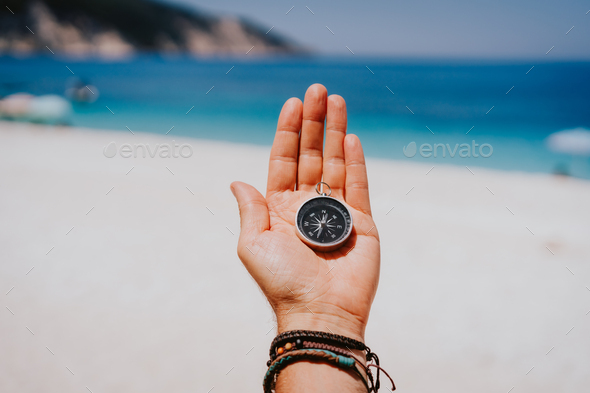 Stretched hand palm with black metal compass against summer beach and blue sea. Follow your way