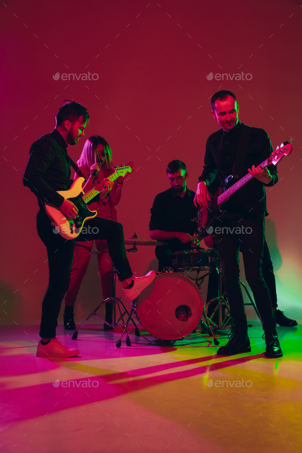 Young caucasian musicians, band performing in neon light on red studio  background Stock Photo by master1305