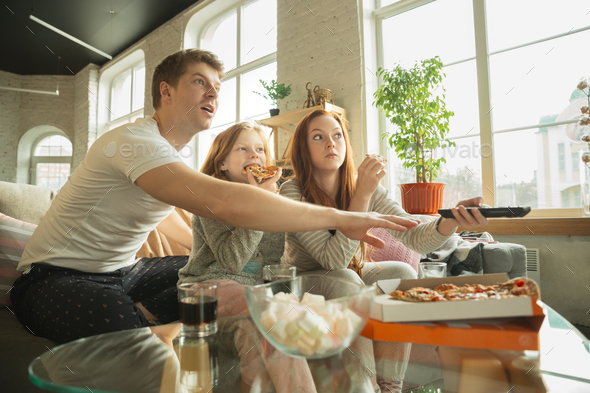 Family spending nice time together at home, looks happy and excited, eating pizza, watching sport