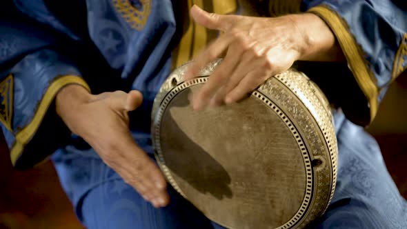 Tight shot of man in Moroccan dress playing arabic doumbek, darbuka, or derbeki alt