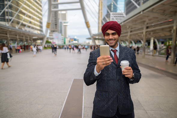Happy Indian businessman outdoors in city using mobile phone