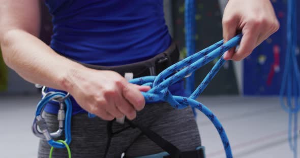 Midsection of caucasian woman securing rope in a harness belt at indoor climbing wall alt