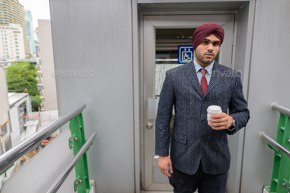 Portrait of Indian businessman with turban outdoors in city holding coffee cup