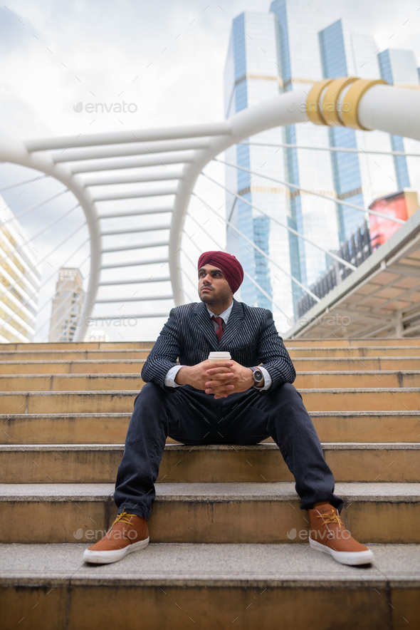 Indian businessman sitting outdoors in city while thinking