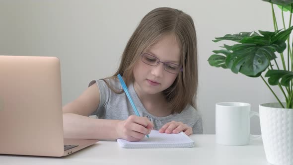 Little School Girl Wearing Glasses Sitting at Table Doing Homework alt