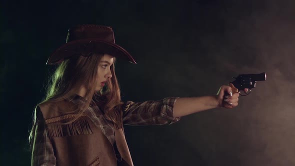 Girl Holds a Revolver in Her Hands and Aiming at the Villain. Black Smoke Background. Slow Motion alt