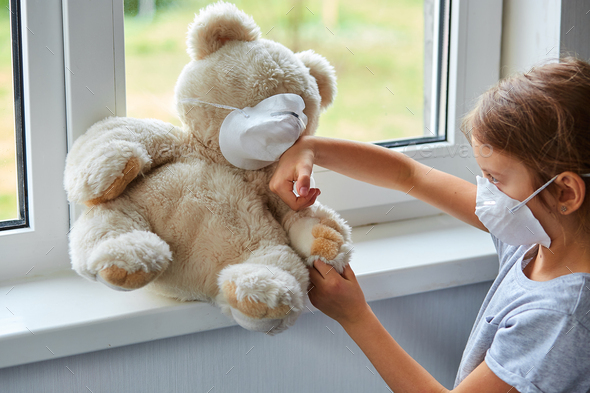 Little girl holding and hugging teddy bear in mask.