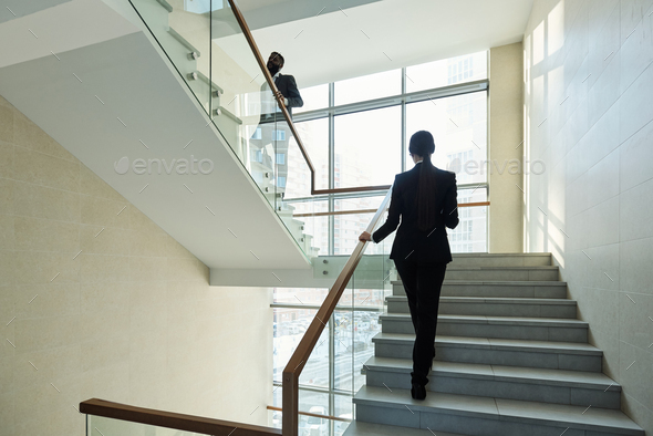 Elegant businesswoman following her African colleague while both moving upstairs