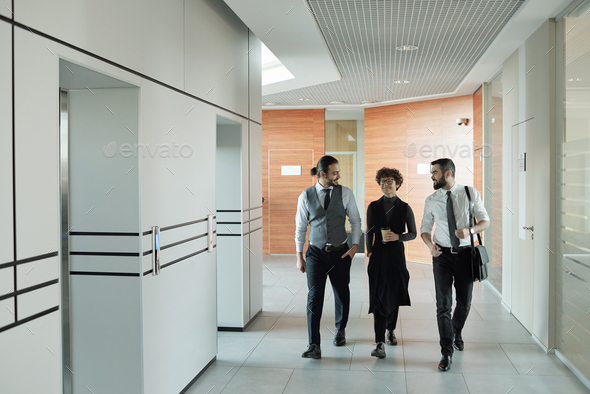 Three young cheerful colleagues in formalwear chatting on their way to office