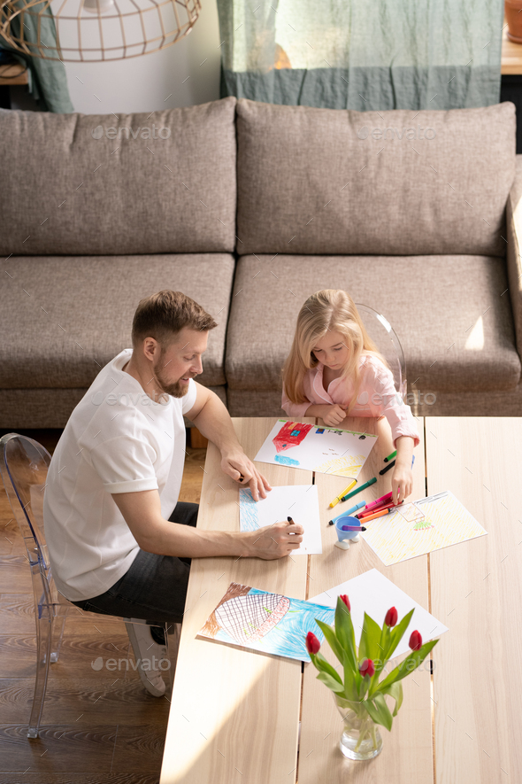 Young man teaching his little daughter how to draw with color pencils