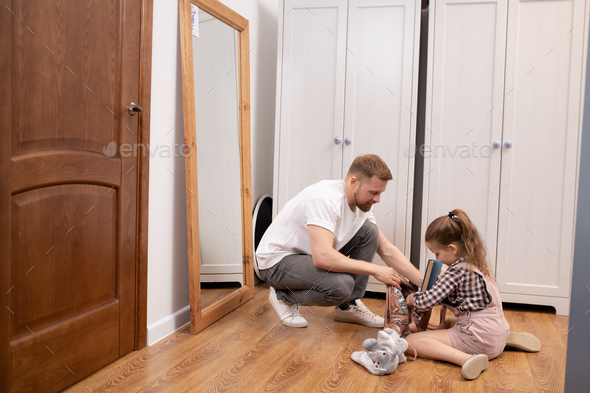 Young father helping his cute little elementary school daughter pack rucksack
