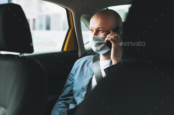 Bald man businessman in medical face mask using mobile phone inside yellow car taxi - Stock Photo - Images