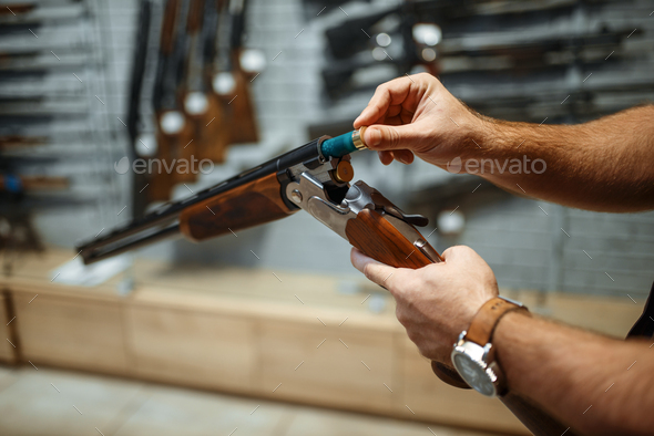 Man loads a rifle, gun shop interior on background