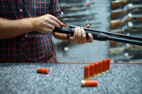 Male person with rifle loads ammo in gun shop
