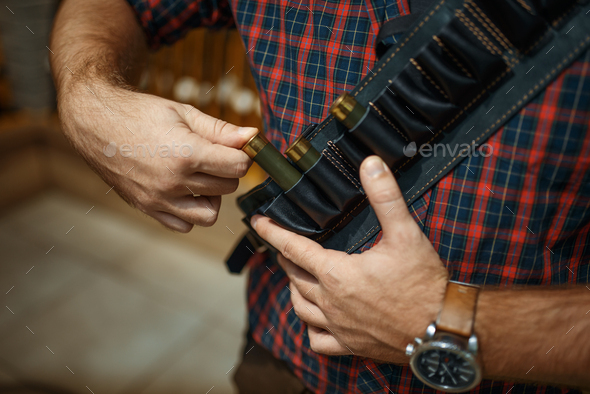 Man in ammo belt, rifles on background, gun shop