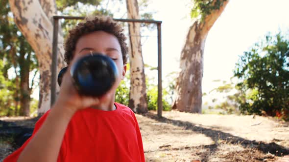 Dehydrated boy drinking water bottle during obstacle course alt
