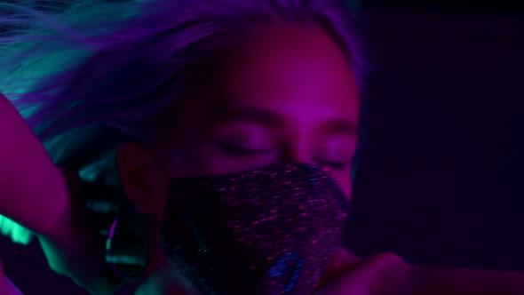 Young Beautiful Fashionable Woman in Protective Mask with Rhinestones Dancing in Bar or Club. Neon alt