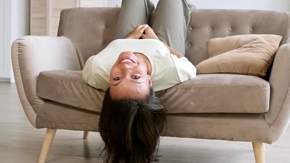 Joyful Young Woman Lying Headlong on Couch alt