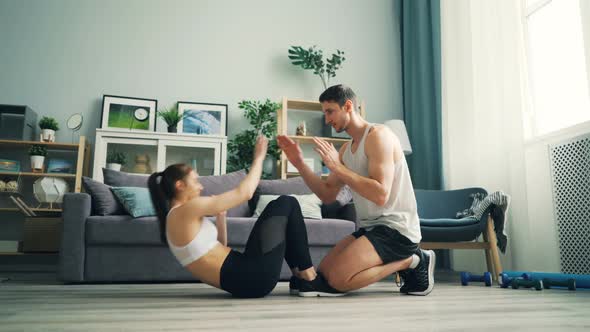 Young People Man and Woman Doing Situps and Clapping Hands Training at Home alt