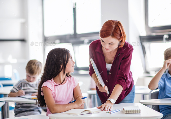 A teacher walking among small school children on the lesson, explaining ...