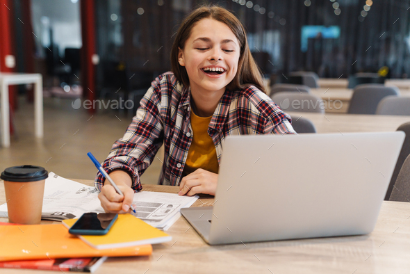 Image of smiling girl doing homework with laptop and exercise books