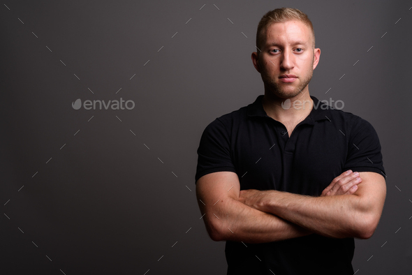 Man with blond hair wearing black polo shirt against gray backgr