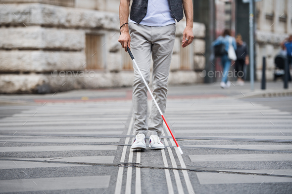 Midsection of young blind man with white cane walking across the street in city