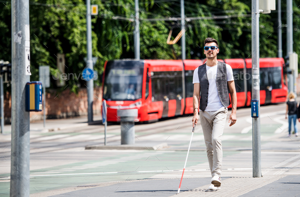 Young blind man with white cane walking across the street in city