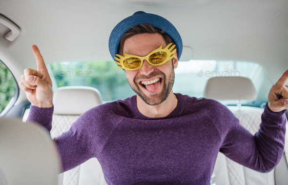 Cheerful man with party accessories sitting in car, having fun - Stock Photo - Images