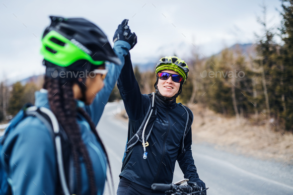 Two mountain bikers standing on road outdoors in winter, giving high five
