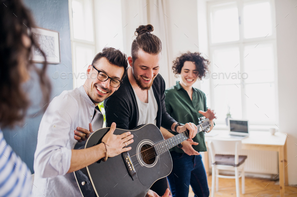 A group of young friends with guitar indoors at home, house sharing concept