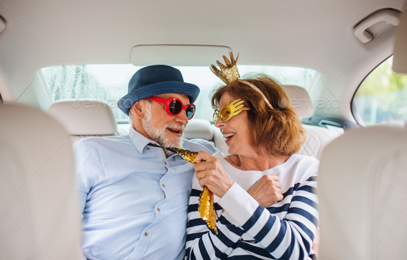 Cheerful senior couple with party accessories sitting in car, having fun - Stock Photo - Images