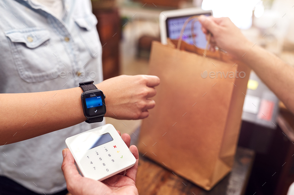 Close Up Of Woman In Store Making Contactless Payment At Sales Desk Holding Smart Watch To Reader