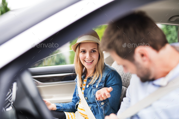 Happy young couple sitting in car, talking