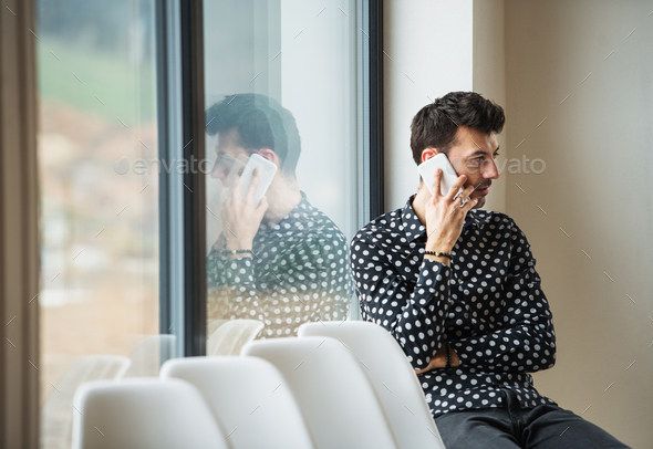 Young man with smartphone sitting by the window, making phone call. Copy space